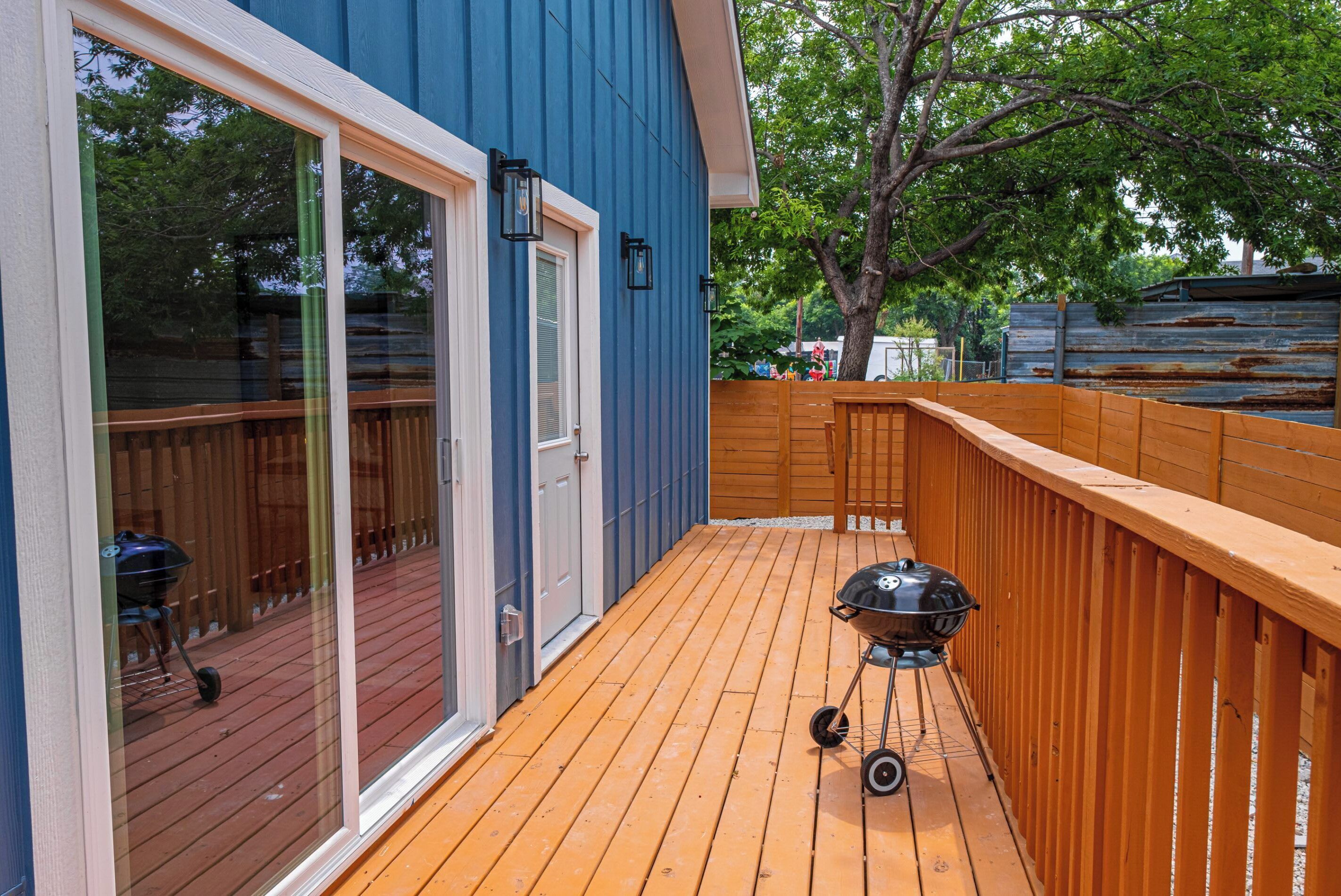 Een terras met een barbecue, houten leuning en een schuifdeur naar een patio.