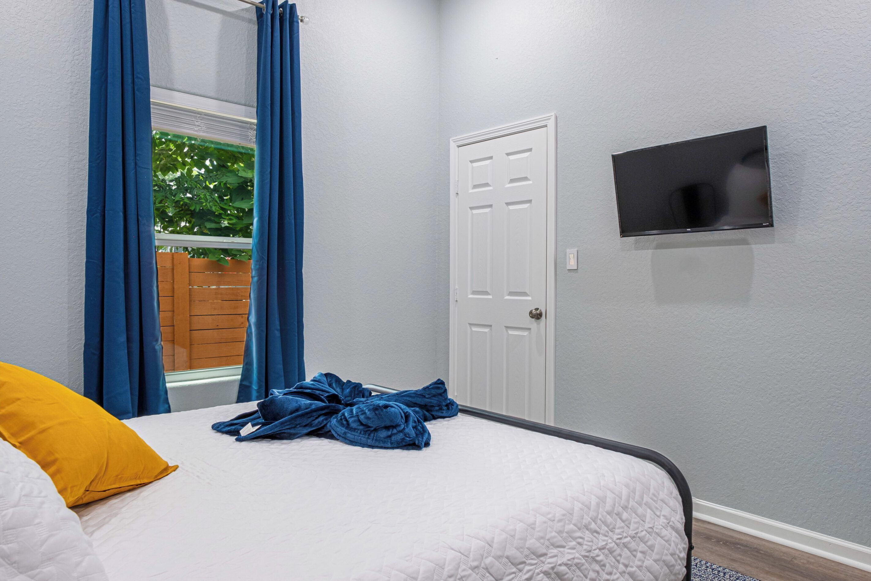 Une chambre à coucher avec un lit, un téléviseur fixé au mur et une fenêtre avec des rideaux.
