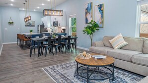 Una sala de estar moderna con un sofá color beige, una mesa de centro redonda y un comedor con una mesa y sillas de madera.