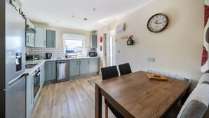 A modern kitchen with stainless steel appliances, a dining area with a wooden table, and a wall-mounted clock.