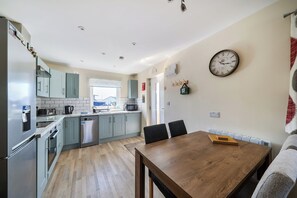 A modern kitchen with stainless steel appliances, a dining area with a wooden table, and a wall-mounted clock. - Seaside Chalet Retreat in Bridlington (Bridlington)