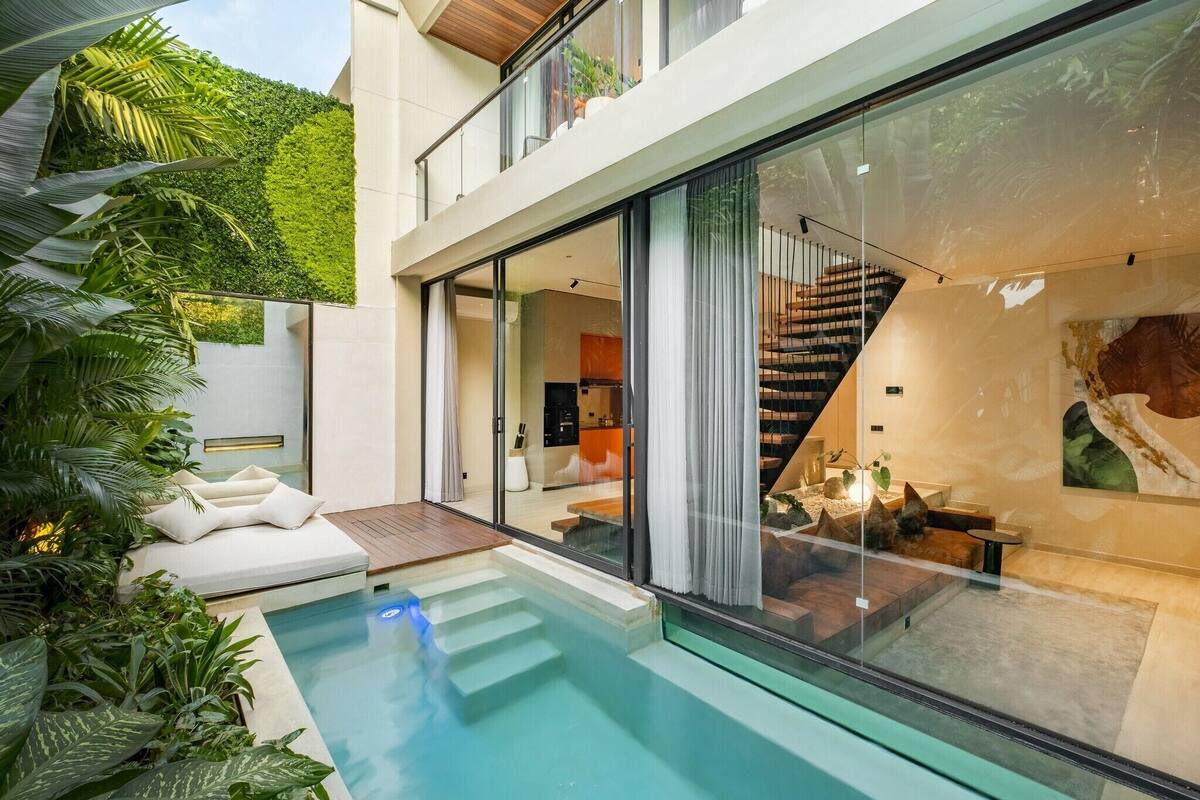 Una casa moderna con piscina cubierta por vidrio, una escalera y un comedor.