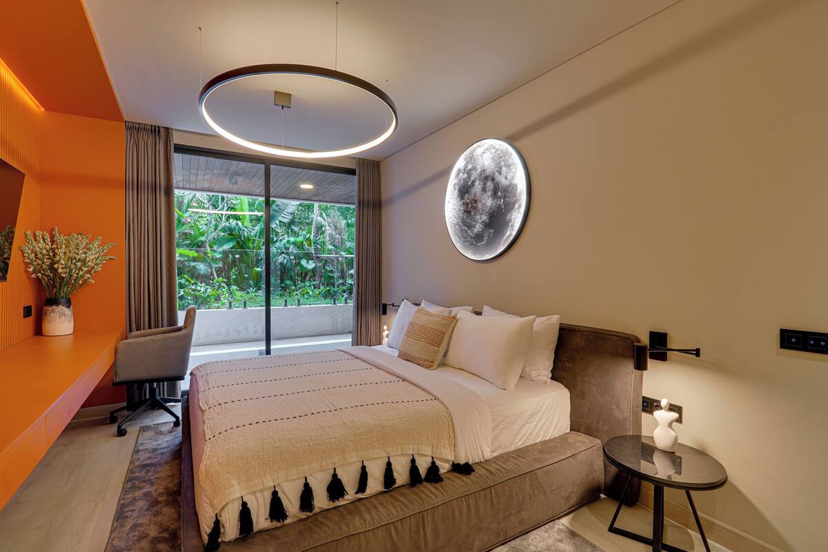 Un dormitorio moderno con una cama grande, un escritorio y vistas a zonas verdes por la ventana.