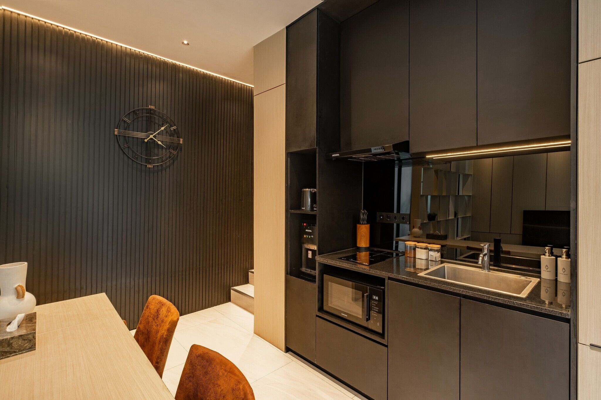 Een moderne keuken met een ingebouwde magnetron, oven en gootsteen. Er is een eethoek met een tafel en stoelen.