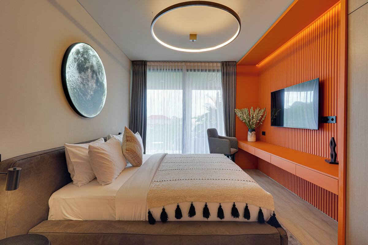 Una habitación de hotel moderna con una cama grande, un televisor de pantalla plana, un escritorio con silla y un amplio ventanal con cortinas.