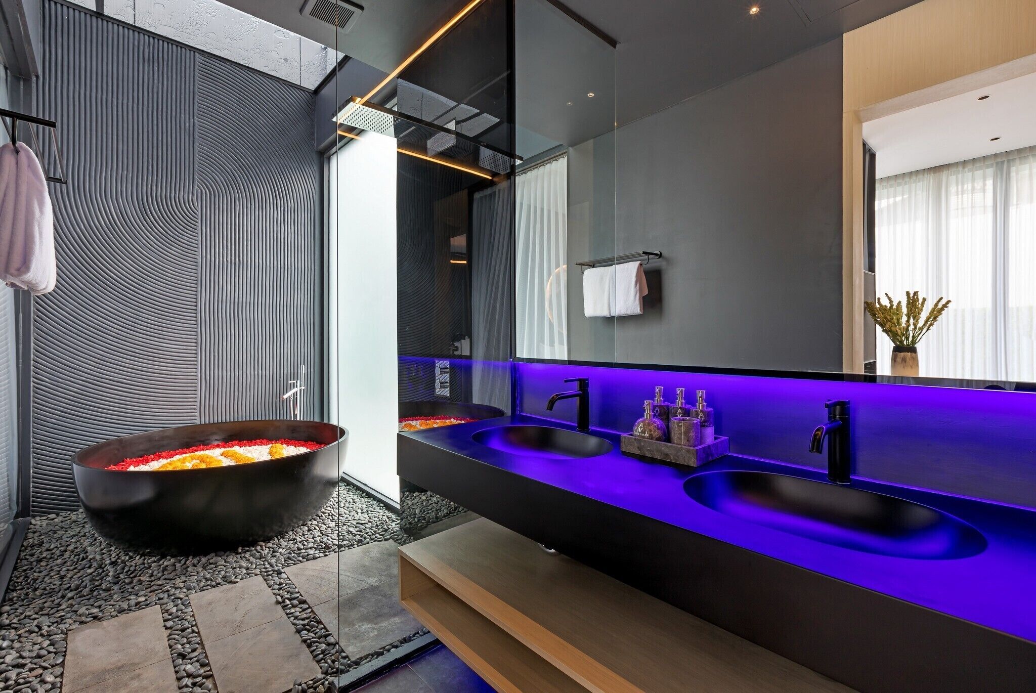 Une salle de bain moderne avec une baignoire noire, deux vasques dotées d’un éclairage bleu sous la surface, et un grand miroir.
