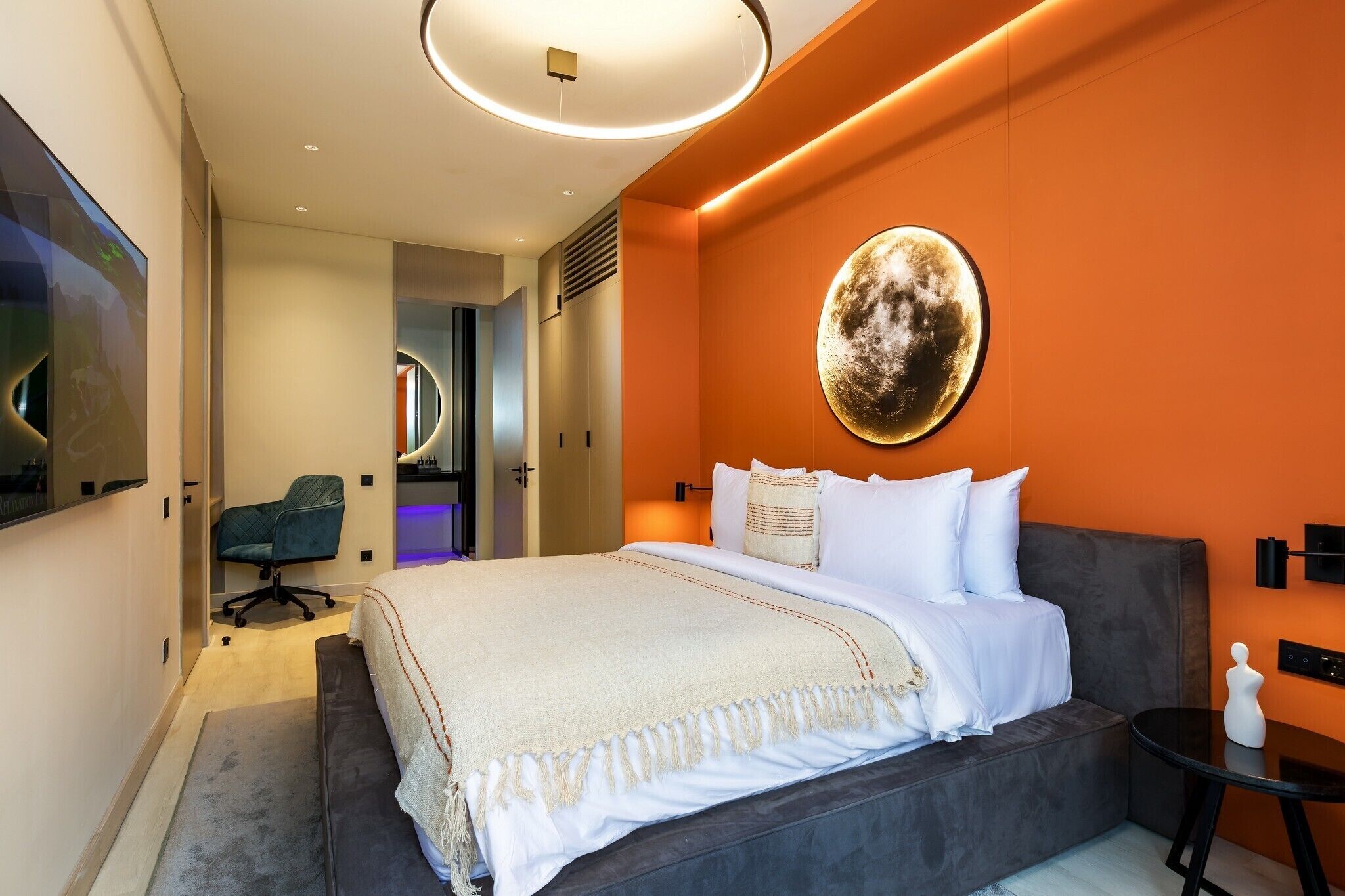 A modern hotel room with a large bed, a round wall decoration, a desk, and a chair.