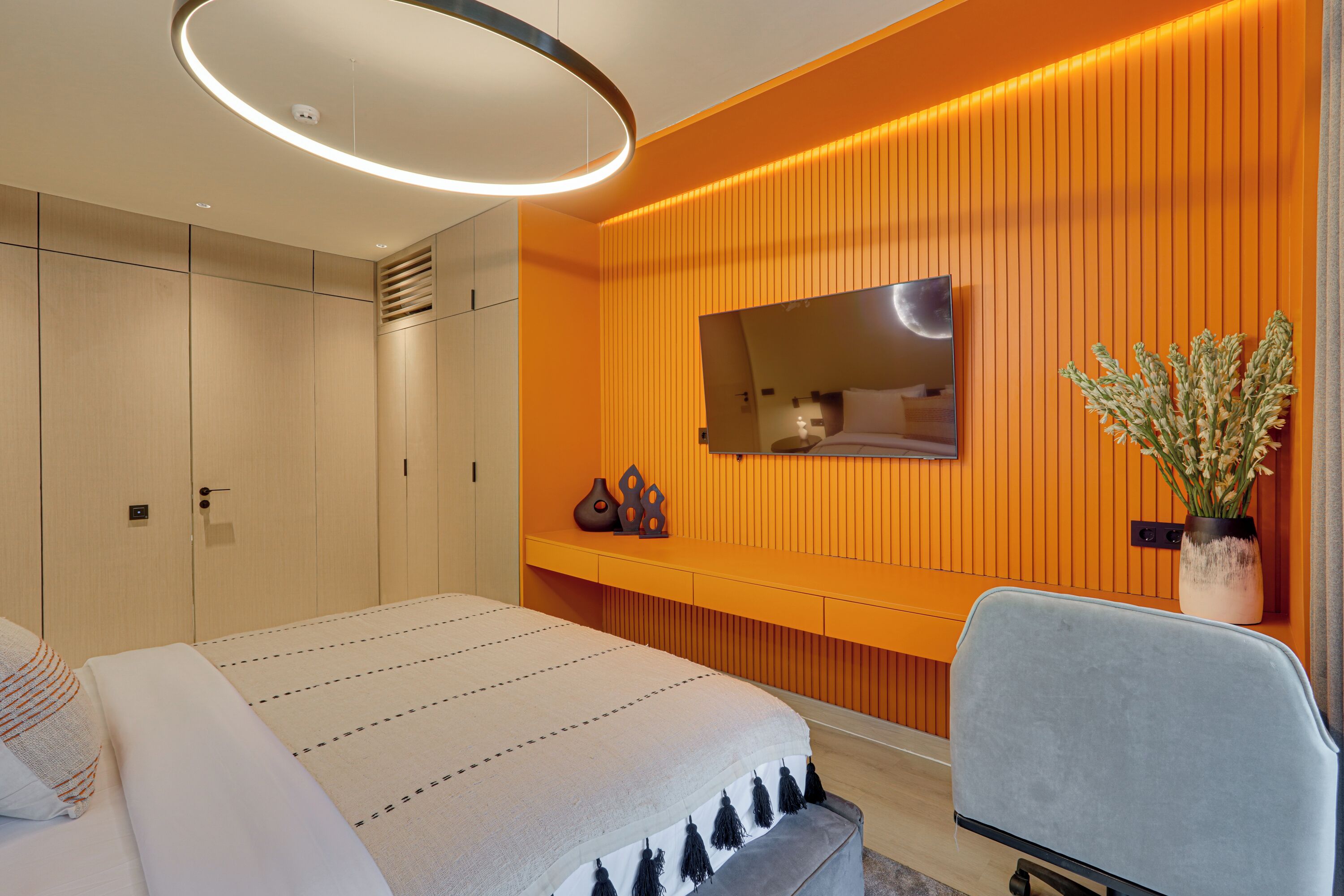 A modern bedroom with a bed, a seating area, a TV, and a potted plant.