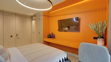 A modern bedroom with a bed, a seating area, a TV, and a potted plant.
