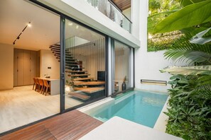 Una casa moderna con una escalera de cristal que lleva a un segundo piso, una piscina y un comedor con suelo de madera.