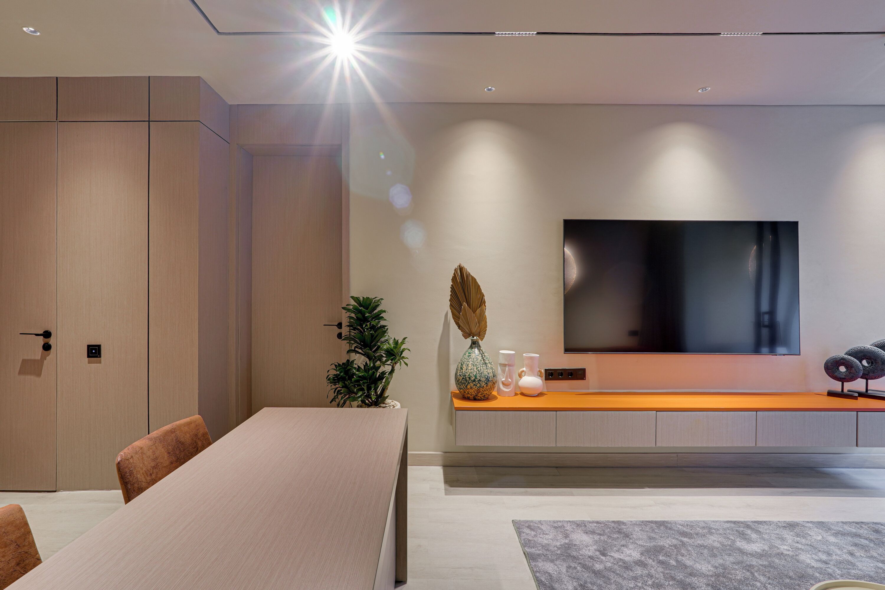 A modern living room with a large flat-screen TV, a wooden dining table, and a seating area.