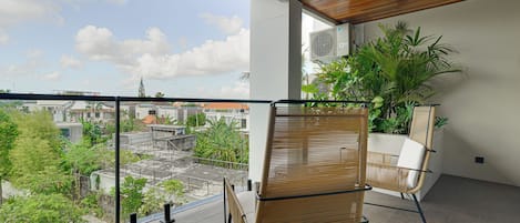 A balcony with a view of the city, a wicker chair, and a potted plant.