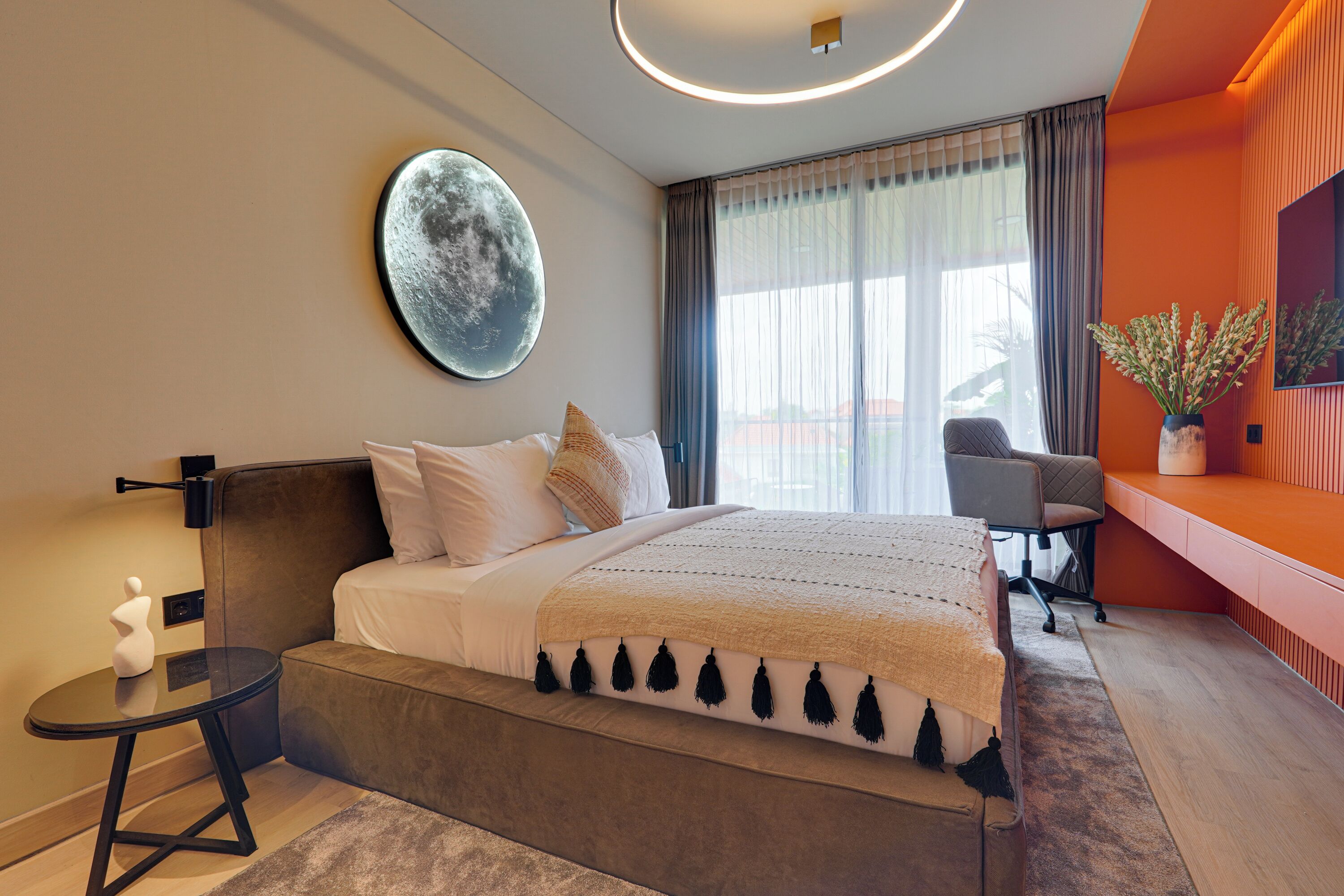 A modern hotel room with a large bed, a round wall decoration, a desk, and a chair.