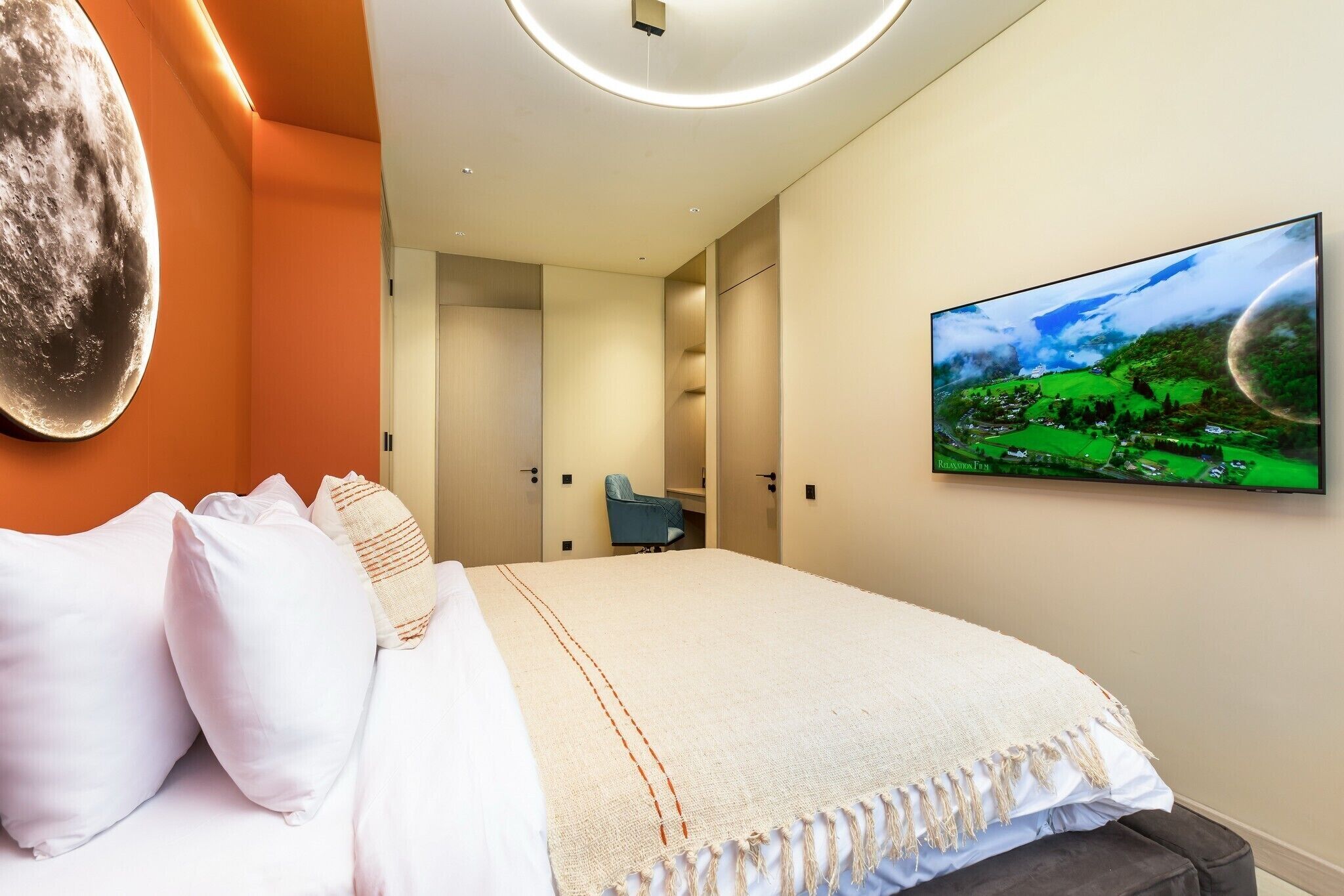 A modern hotel room with a large bed, a flat-screen TV on the wall, and a view of a green landscape.