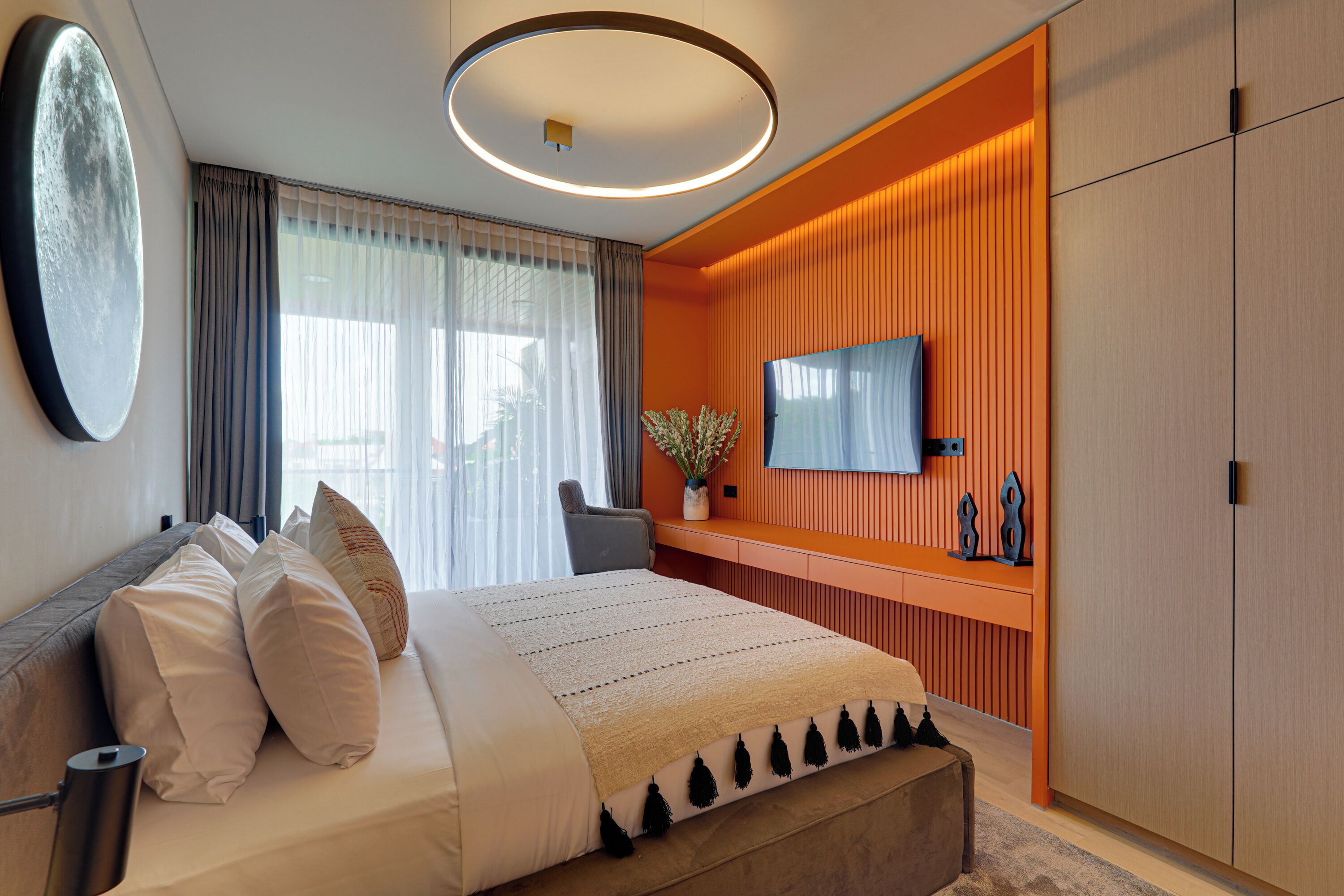 Ein modernes Schlafzimmer mit einem großen Bett, einem an einer orangefarbenen Wand montierten Fernseher und einem Holzschrank.