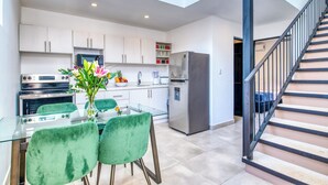 Una cocina moderna con armarios blancos, electrodomésticos de acero inoxidable, una mesa de comedor de vidrio con sillas verdes y una escalera con barandillas negras.