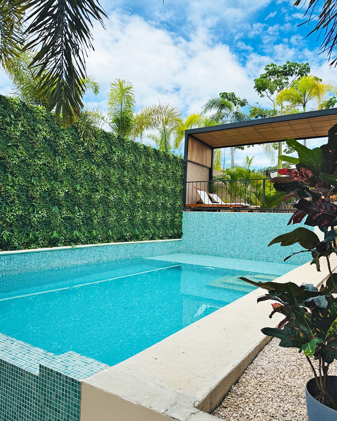 Una piscina con agua cristalina azul, rodeada por un borde de azulejos y una barandilla de concreto.