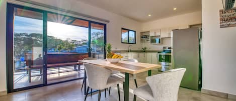 A modern kitchen with a dining area, large windows, and a view of the outdoors.