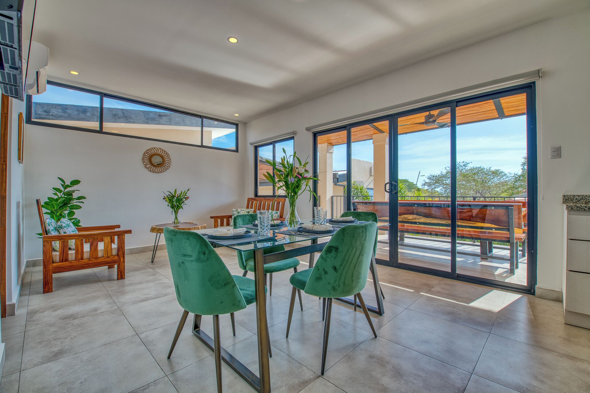 A spacious dining area with a glass table and green chairs, large windows, and a view of the outdoors.