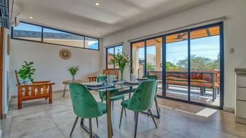 A spacious dining area with a glass table and green chairs, large windows, and a view of the outdoors.