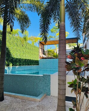 A swimming pool with a tiled edge, surrounded by palm trees and a landscaped garden. - Muna Tamarindo (Tamarindo)
