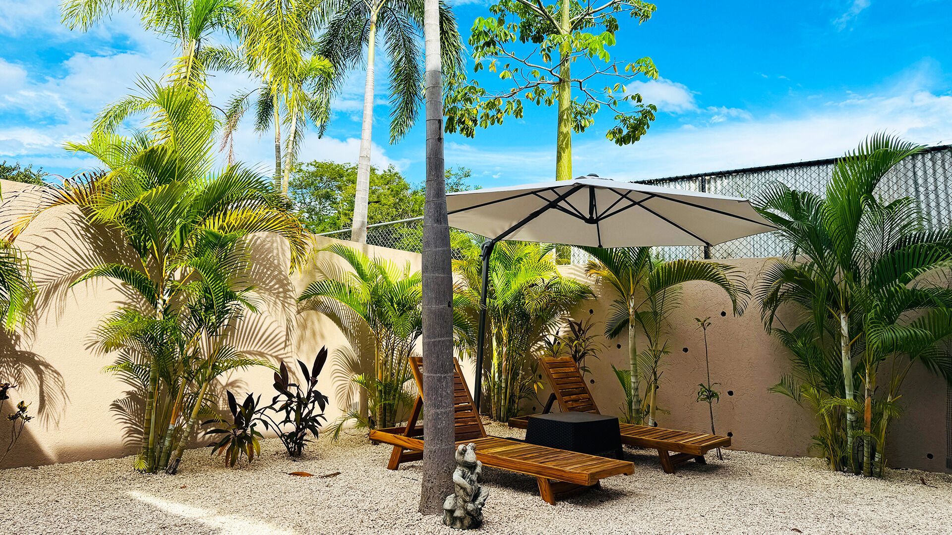 Un área de estar al aire libre con ambiente tropical, que incluye una pérgola, sillas reclinables y varias palmeras.