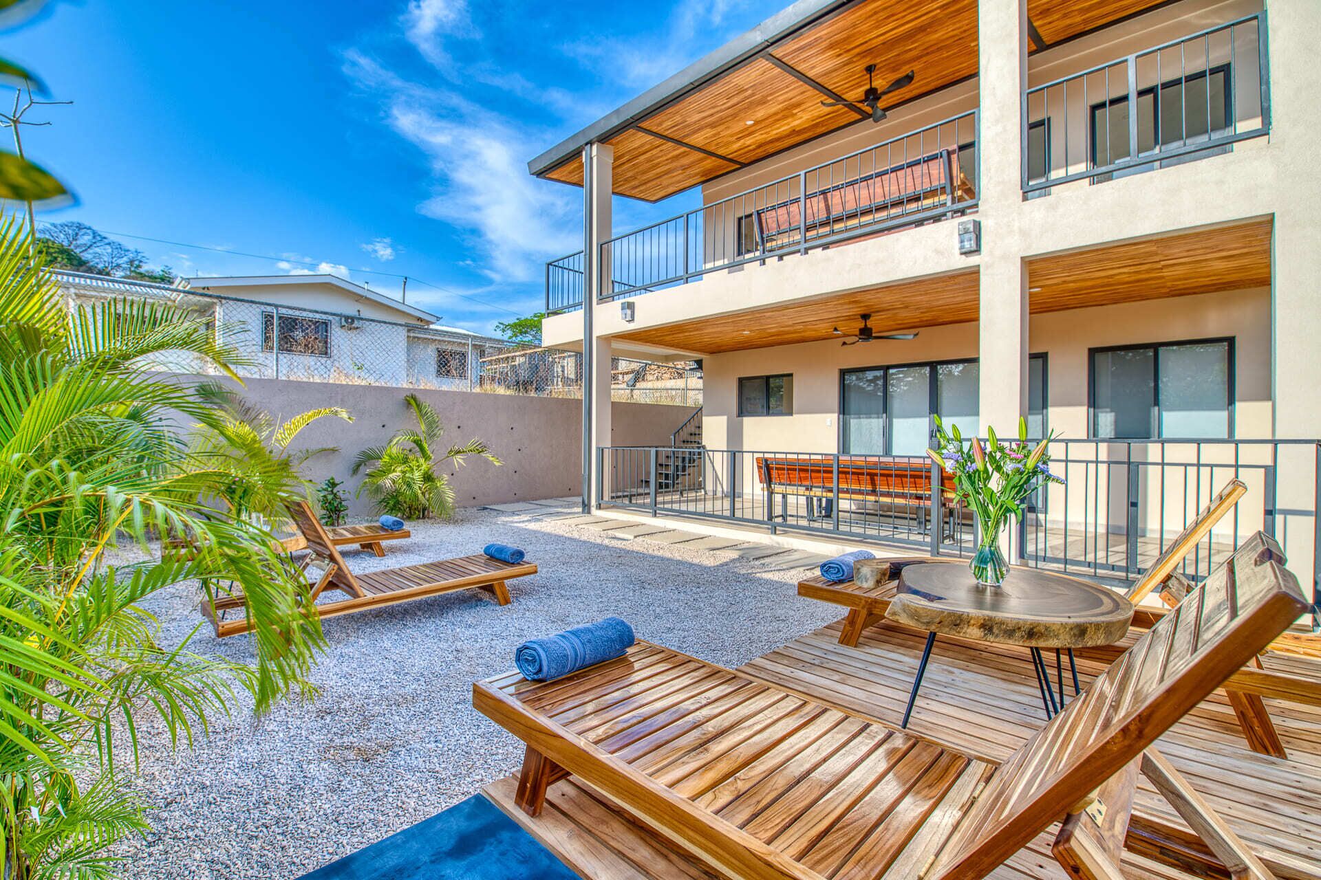 Un espacio exterior moderno con sillones de madera y una mesa, rodeado por un patio de grava.