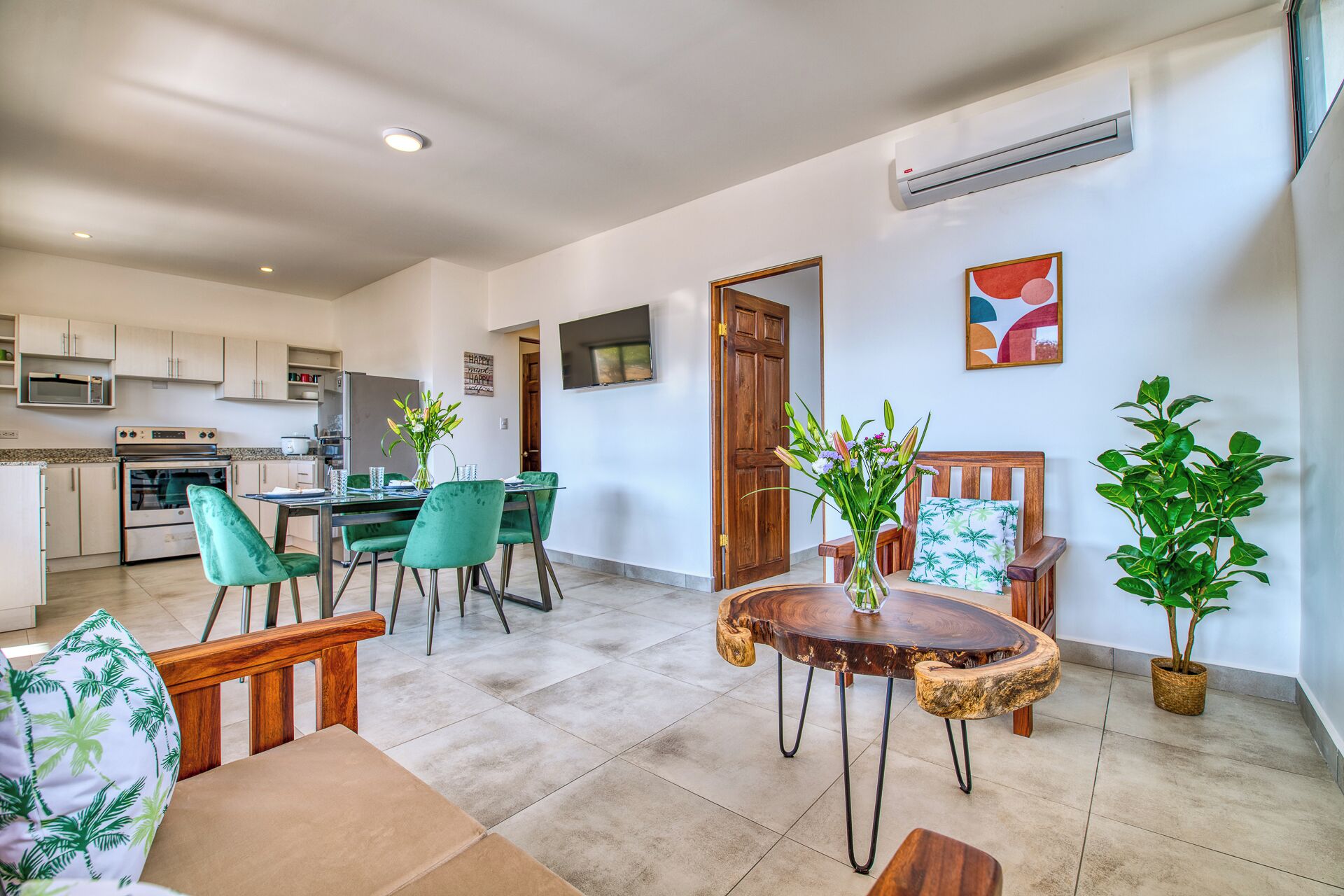 A modern kitchen with white cabinets, a built-in oven, and a dining area with green chairs and a wooden table.
