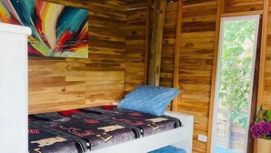 A bunk bed with a colorful abstract painting above it, a window with a view of greenery, and a woven rug on the floor. - Family room in a beachfront cabin - Barú (Cartagena)