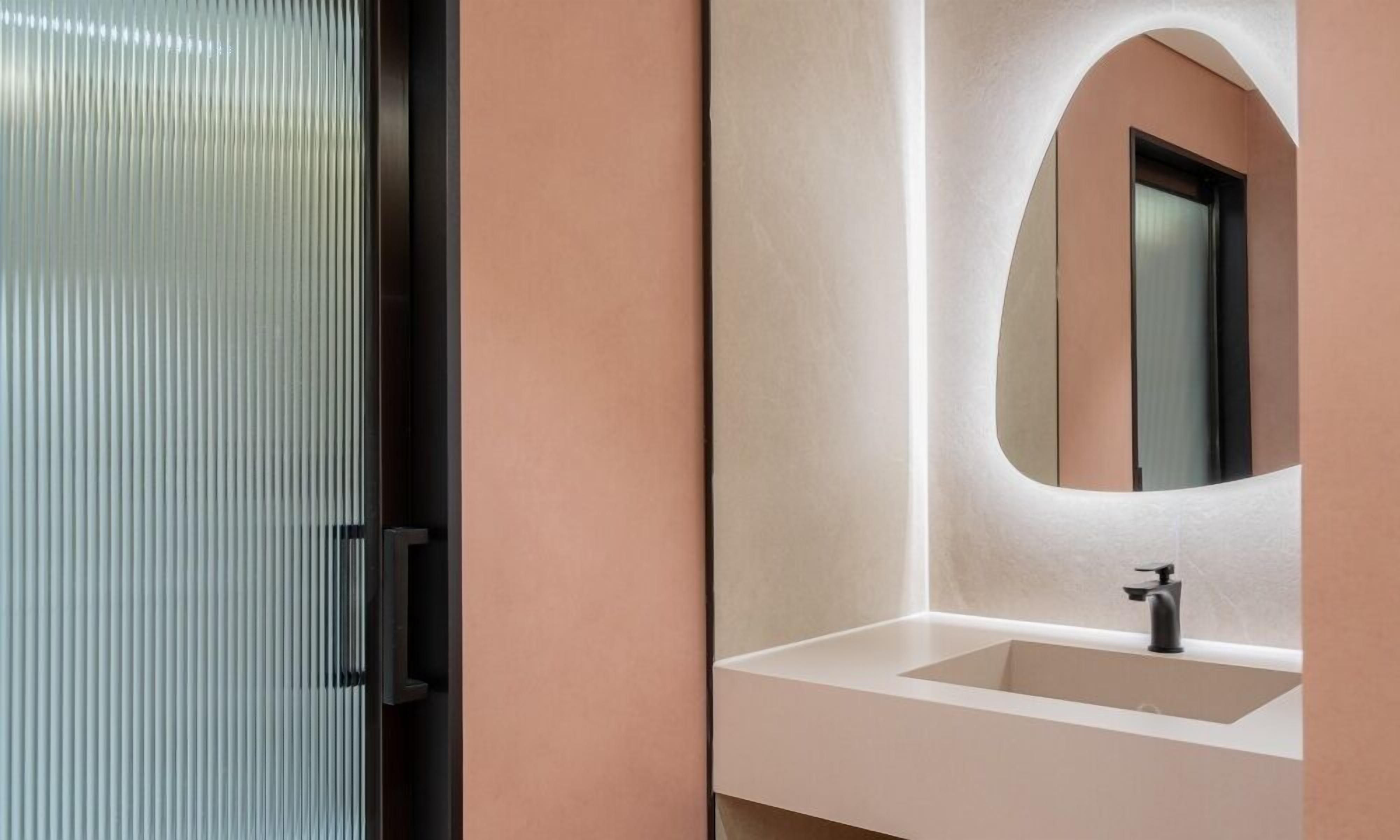 A bathroom with a glass door, a white sink, and a mirror with an arch design.