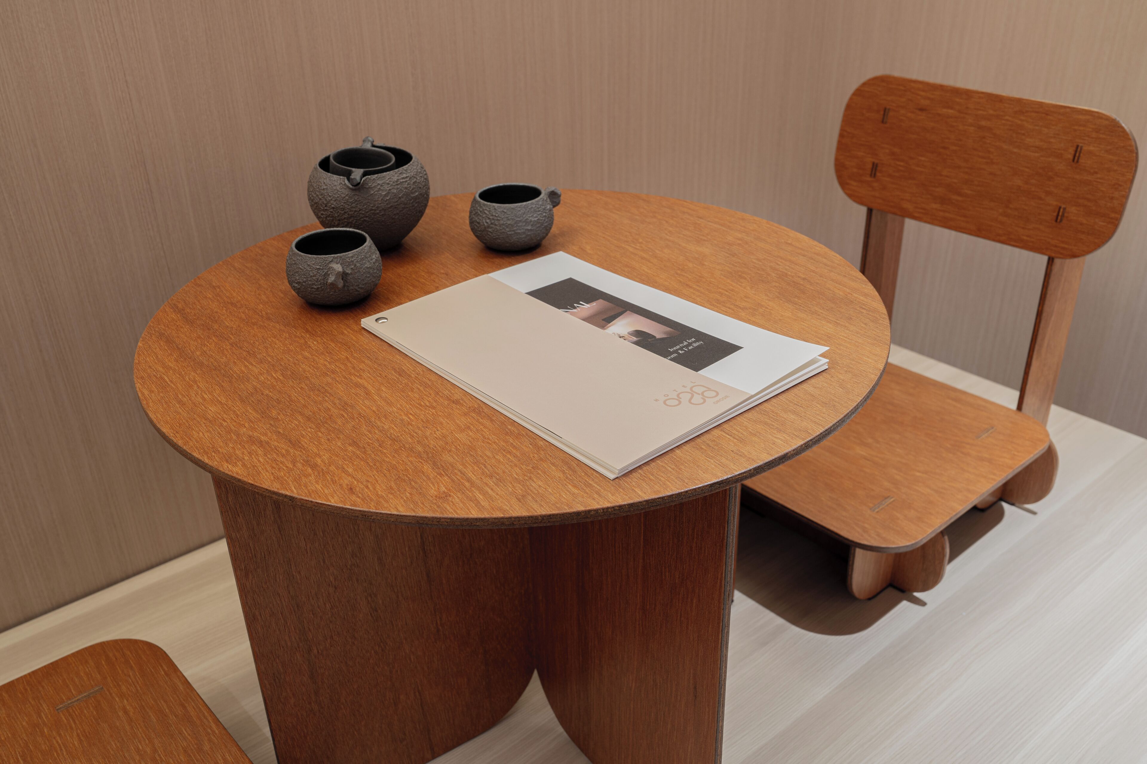 Uma mesa de madeira redonda com uma revista, dois pequenos vasos e uma cadeira.
