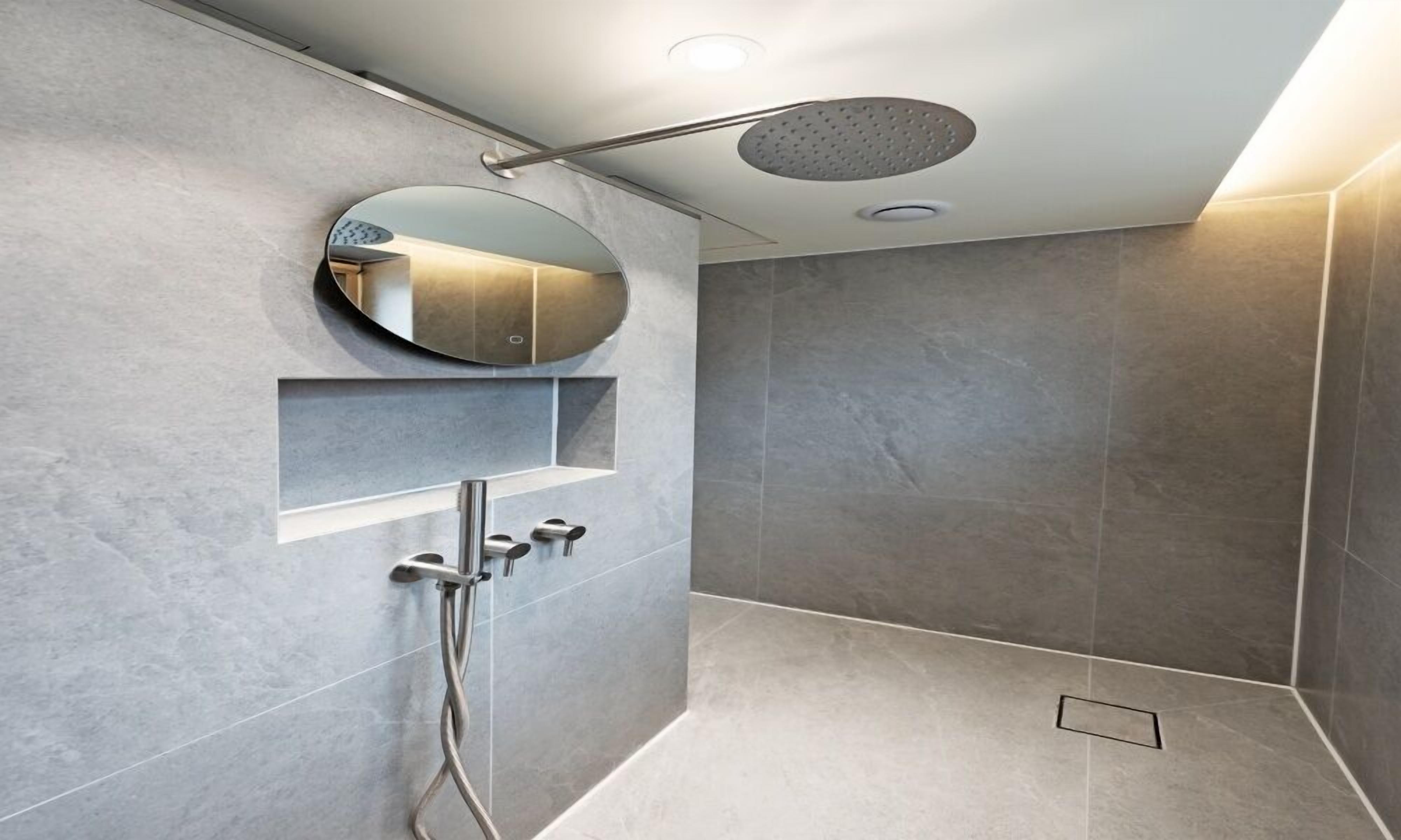 A modern shower with a round mirror, a handheld showerhead, and a wall-mounted control panel.