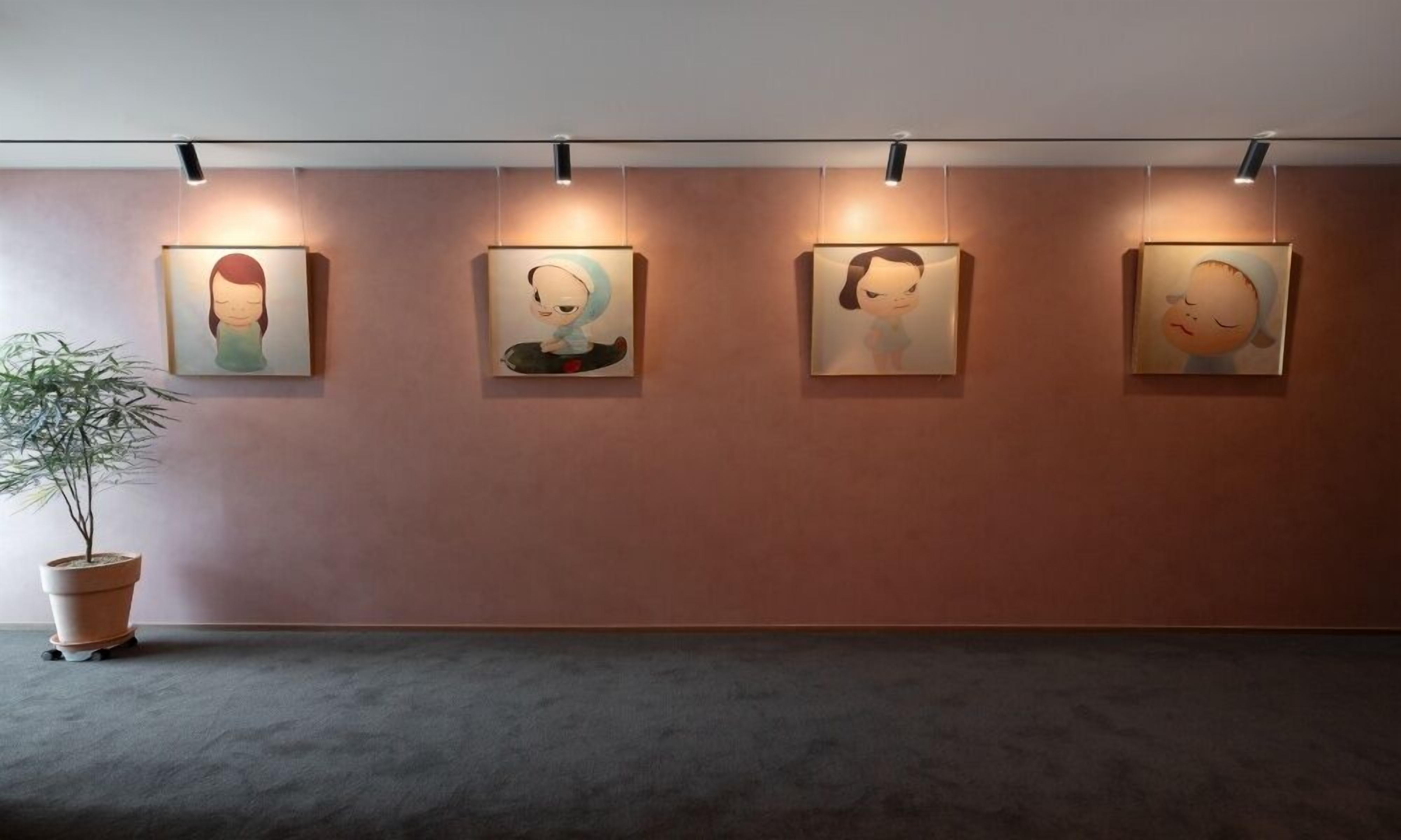 A gallery wall with four framed artworks, a potted plant, and a grey carpeted floor.