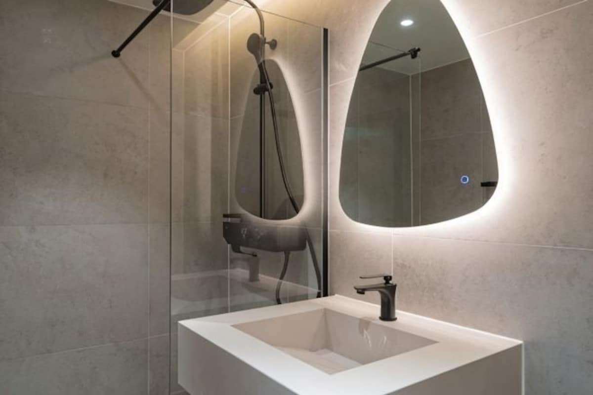 A modern bathroom with a glass enclosure, a bathtub, a large mirror, and a white sink.
