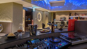 Un espace bar moderne doté d’une console de DJ, d’un grand écran diffusant une image céleste, ainsi que d’un assortiment de bouteilles et de verres.