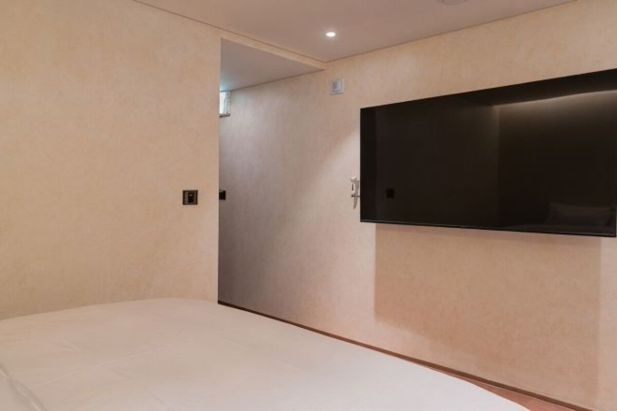 Une chambre d’hôtel avec un lit, un téléviseur fixé au mur et une porte donnant sur une autre pièce.