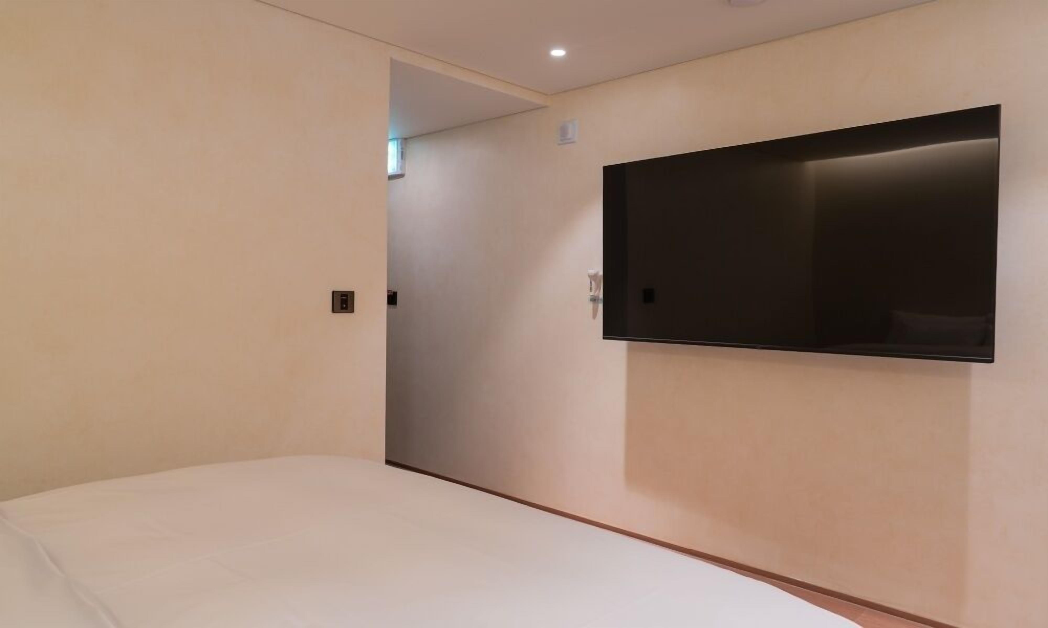 A modern hotel room with a single bed, a flat-screen TV mounted on the wall, and a door leading to another room.