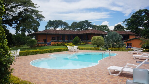 Una piscina con borde de baldosas, rodeada de sillones blancos y un edificio con tejado de cerámica.
