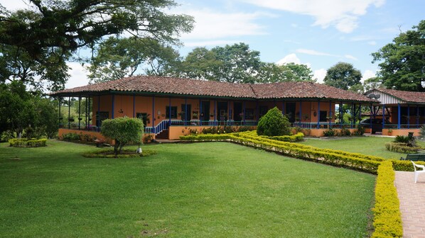 A two-story building with a tiled roof and a covered porch. There is a well-maintained lawn with trimmed bushes and a small tree.