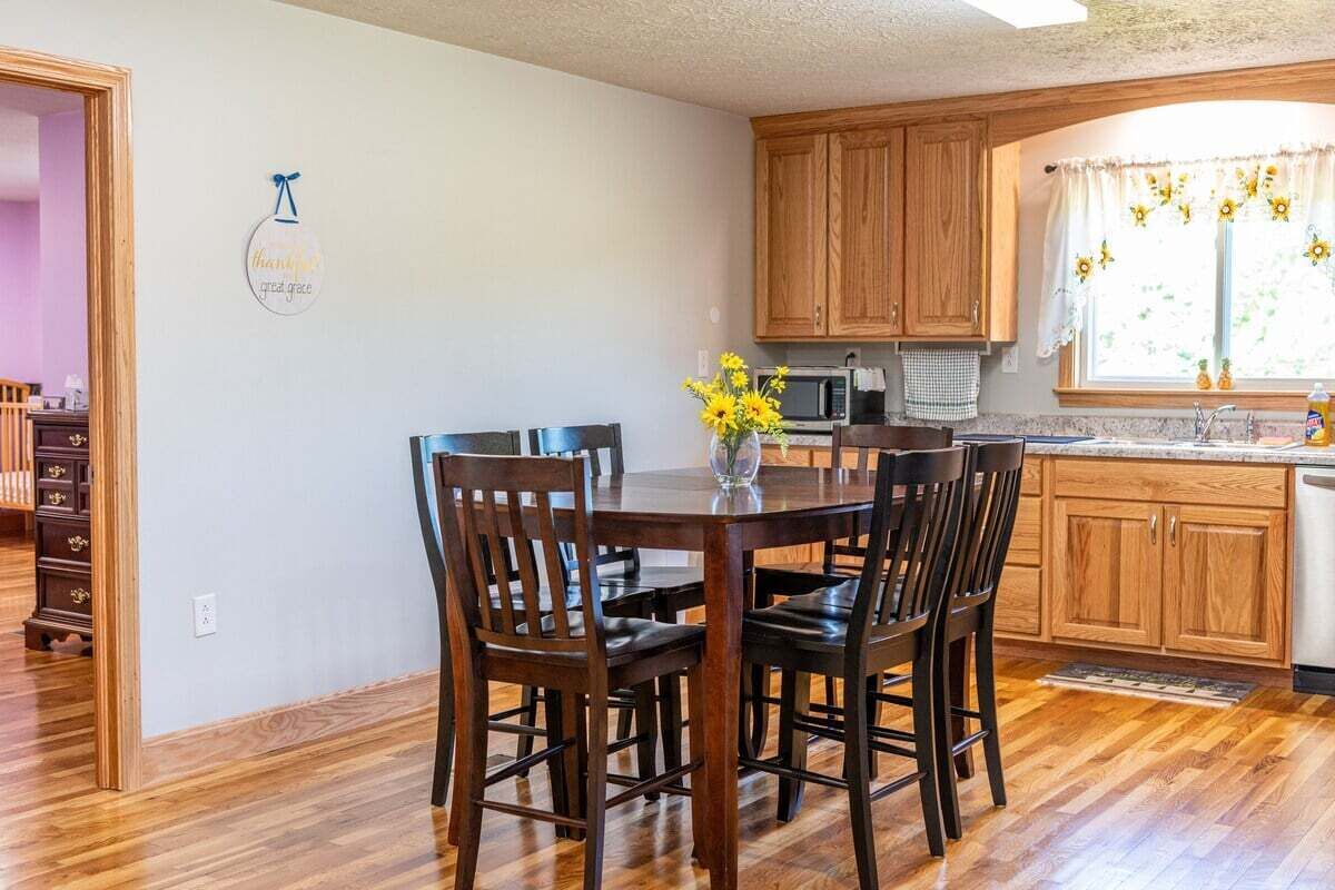 A dining area with a wooden table and chairs, a vase with flowers, and wooden cabinets.
