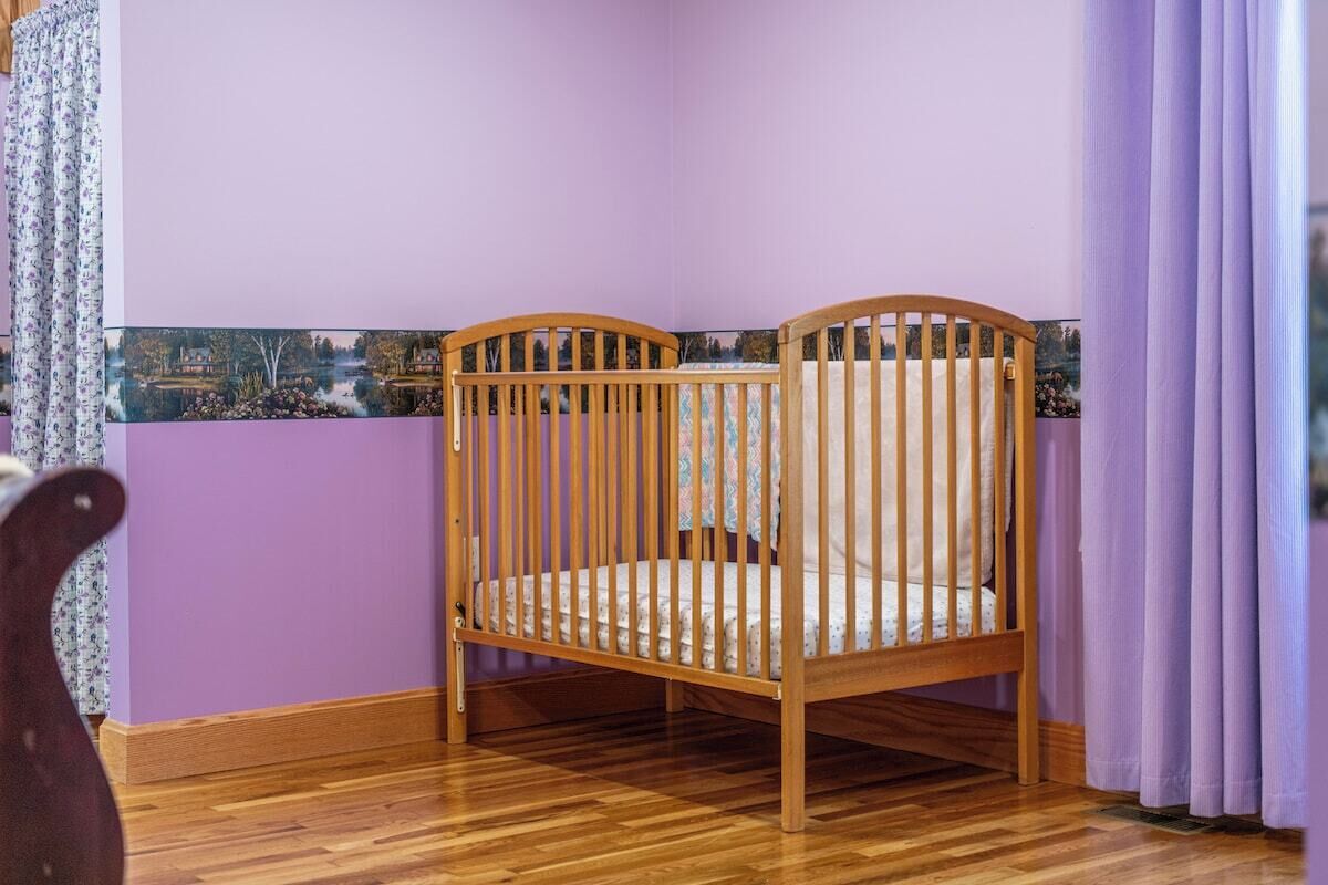 Una cuna de madera en una habitación con paredes moradas y suelo de madera.