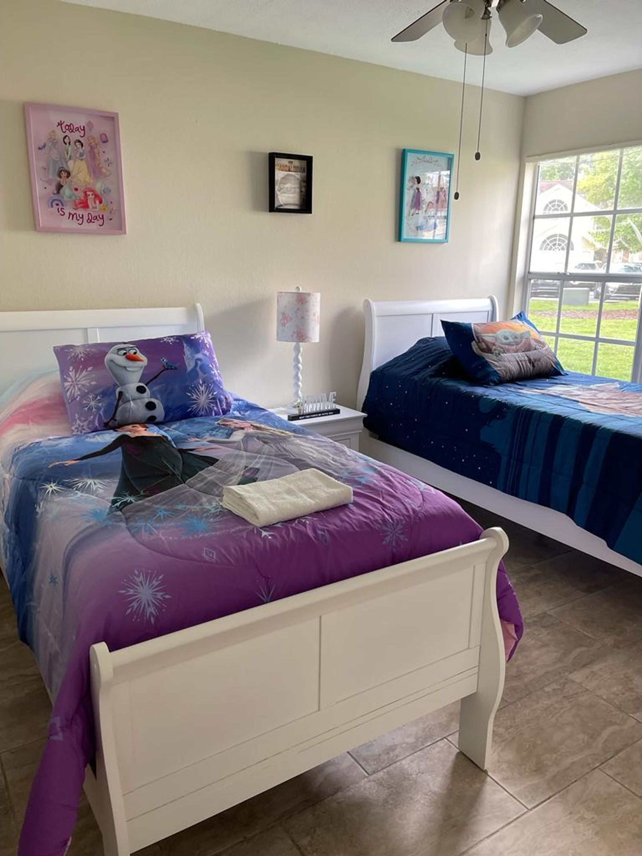 A bedroom with two beds, a nightstand, a lamp, and a window with a view of the outdoors.