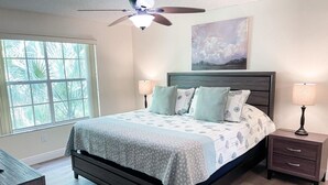 A bedroom with a bed, two bedside tables, a ceiling fan, a window, and a painting on the wall. - Luxury Condo Apartment Near Disney Universal 12 (Kissimmee)