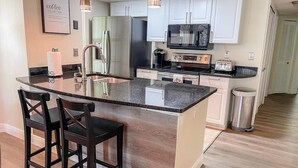 A modern kitchen with a central island, stainless steel appliances, and a bar stool seating area. - Luxury Condo Apartment Near Disney Universal 12 (Kissimmee)
