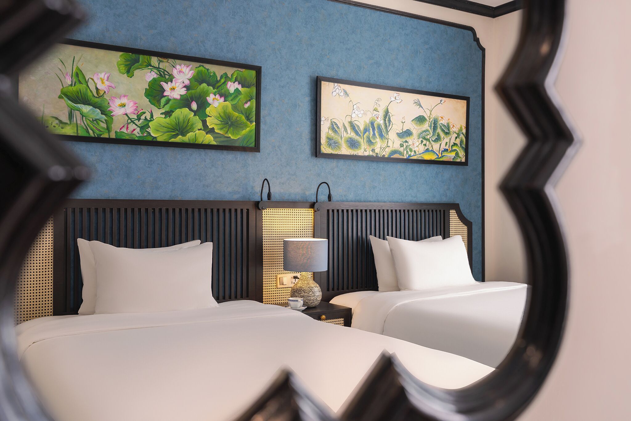 Une chambre d’hôtel avec deux lits, un grand miroir et deux tableaux accrochés au mur.