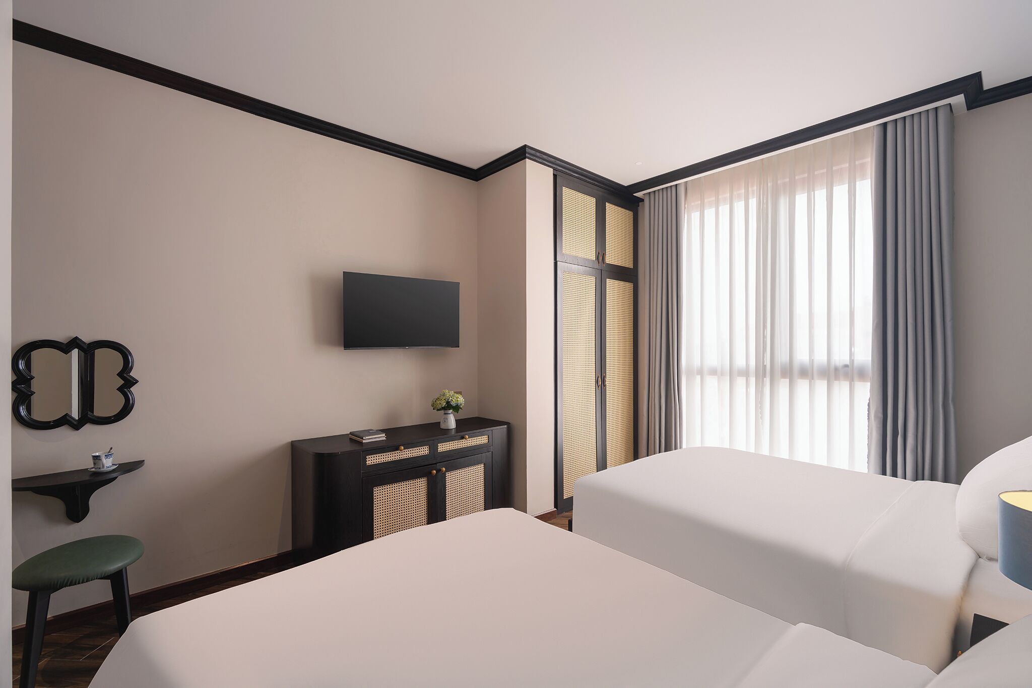 Habitación de hotel con dos camas, televisión, una mesita con un florero y ventana con cortinas.