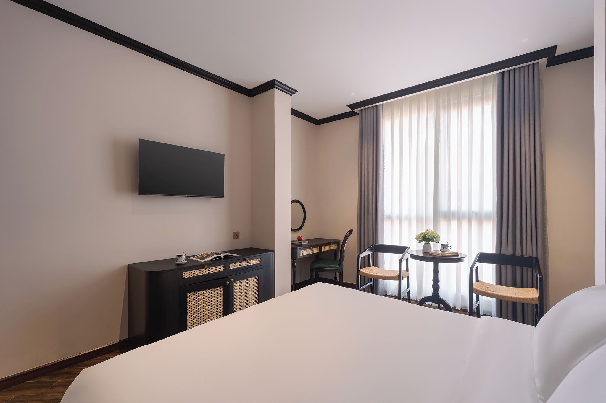 Hotellihuone, jossa on sänky, työpöytä, kaksi tuolia, televisio ja ikkuna, jossa on verhot.