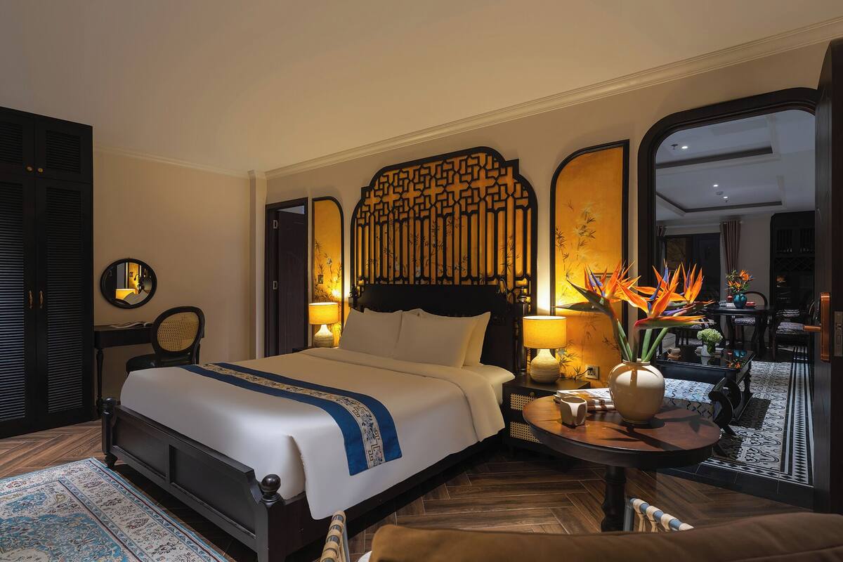 A hotel room with a large bed, bedside tables, a mirror, and a view of the adjacent room.