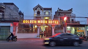 Das Außergebäude des Golden Moon Hotels mit einer auffälligen Neonreklame, einem verschlossenen Eingang und einem Motorrad davor.