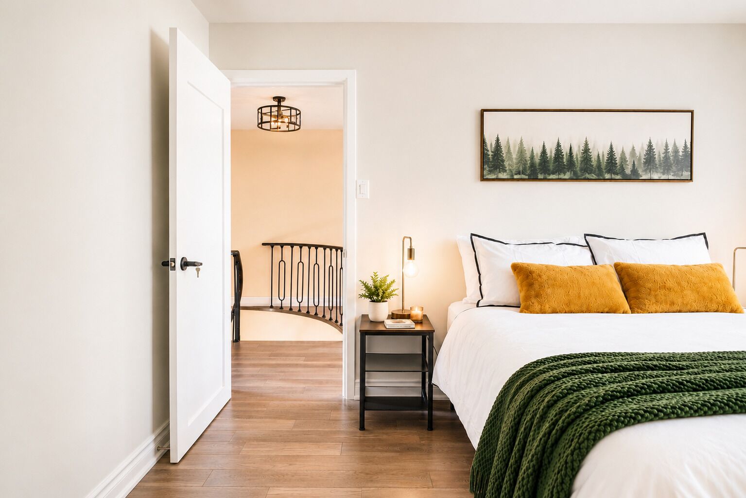 Un dormitorio con una cama, una mesita de noche, una lámpara, un cuadro y una escalera que lleva a otra habitación.